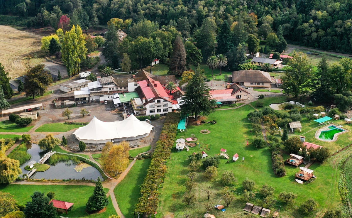 An aerial view of white-painted building with red roofs and a large expanse of bright green grass.