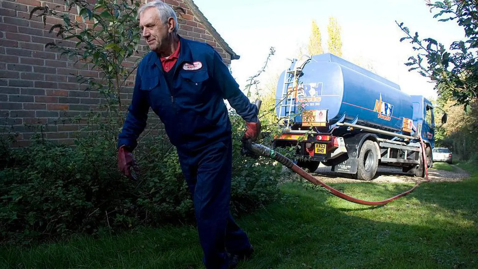  Tanker driver Bill Webb, dressed in blue overalls and carrying a large pipe that is connected to the tanker, delivers domestic heating oil to a house in Newbury in 2007.