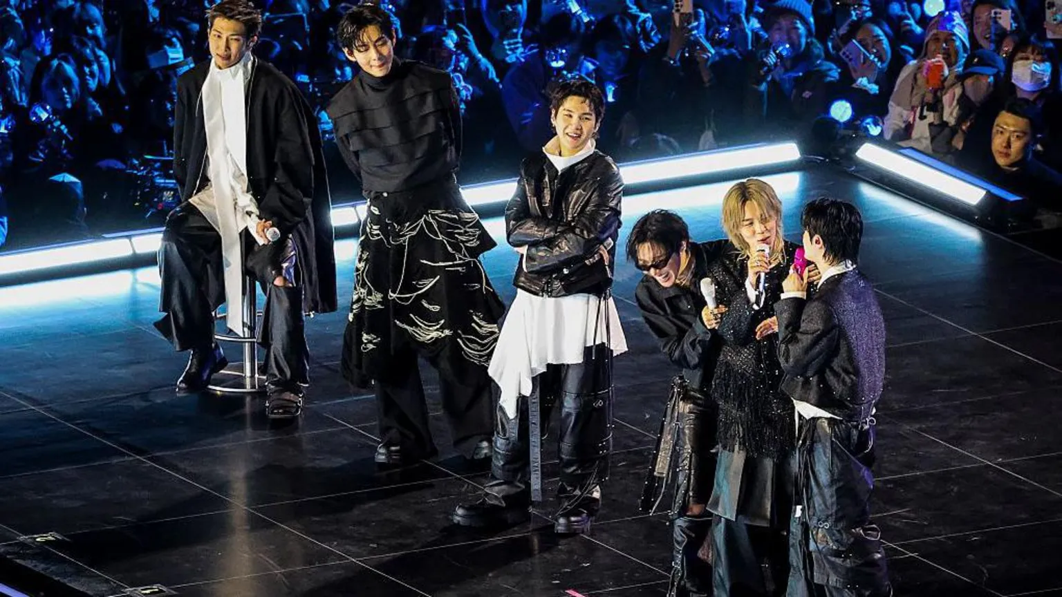  RM, seated, while V, Suga, J-Hope Jimin and Jin stand on stage at the comeback show . 