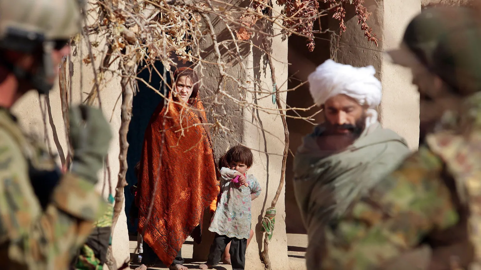 /The Age A girl in an orange blanket and a young child look on as Australian forces patrol a town in Afghanistan