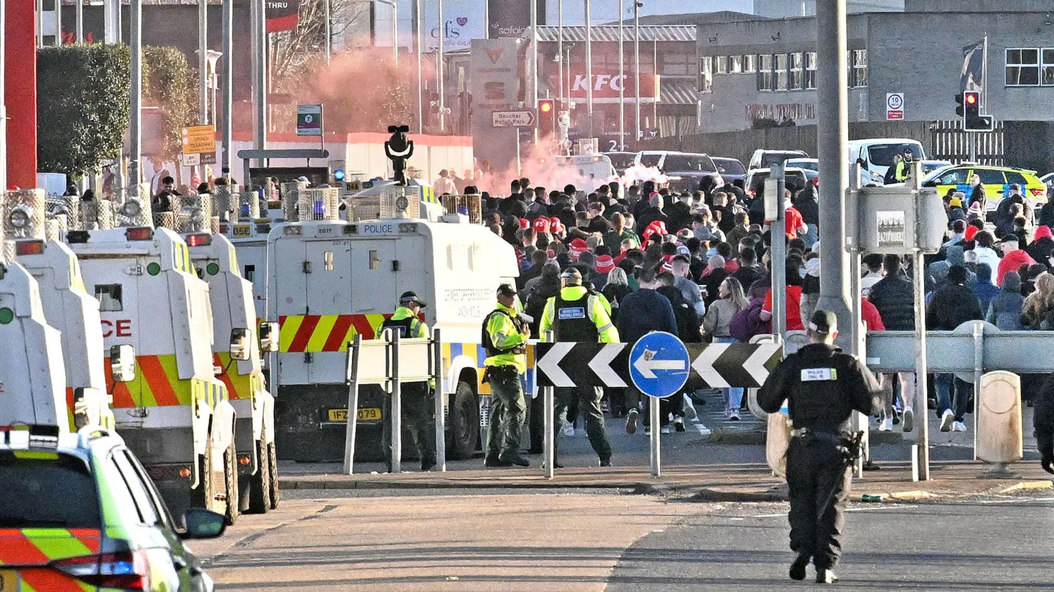 Alan Lewis / PhotopressBelfast Police landrovers parked on a street which is barricaded off. Beyond the barricade a large group of fans are seen walking along the street and some faint red falre smoke can be seen.
