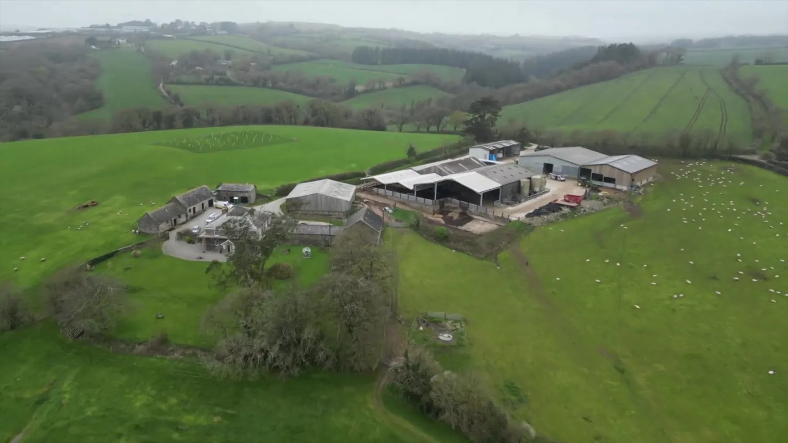 Smeaton Farm near Saltash is seen from above, with various barns and outbuildings seen scattered across an area surrounded by green fields and hedgerows.