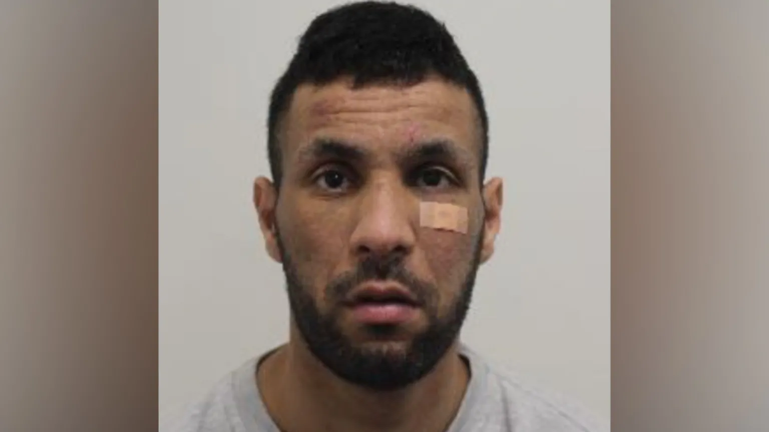 Met Police A head‑and‑shoulders image of a man looking at the camera, with short dark hair, facial hair and a small bandage beneath one eye, set against a plain background.