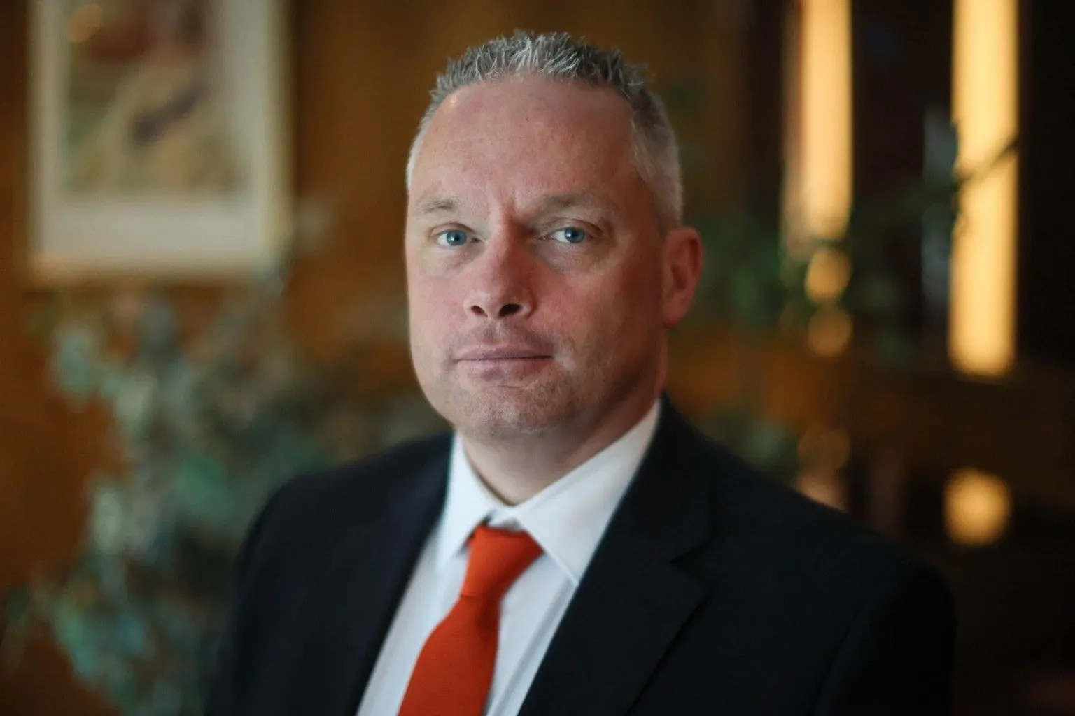 A man with short grey hair and wearing a suit with a red tie