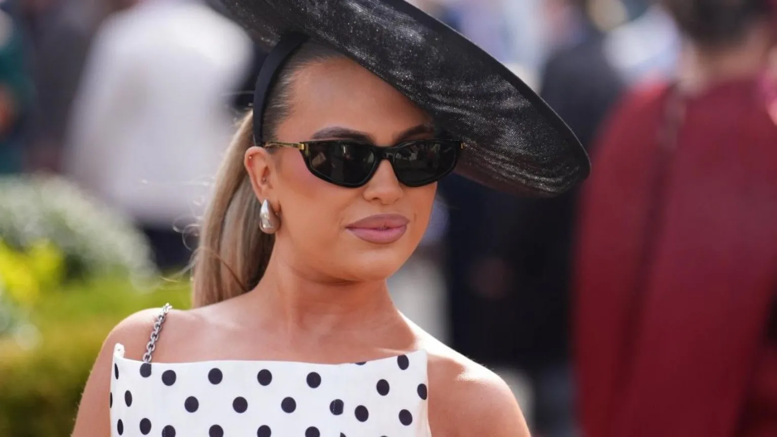 A woman in a white and black polka dot dress and black fascinator and sunglasses