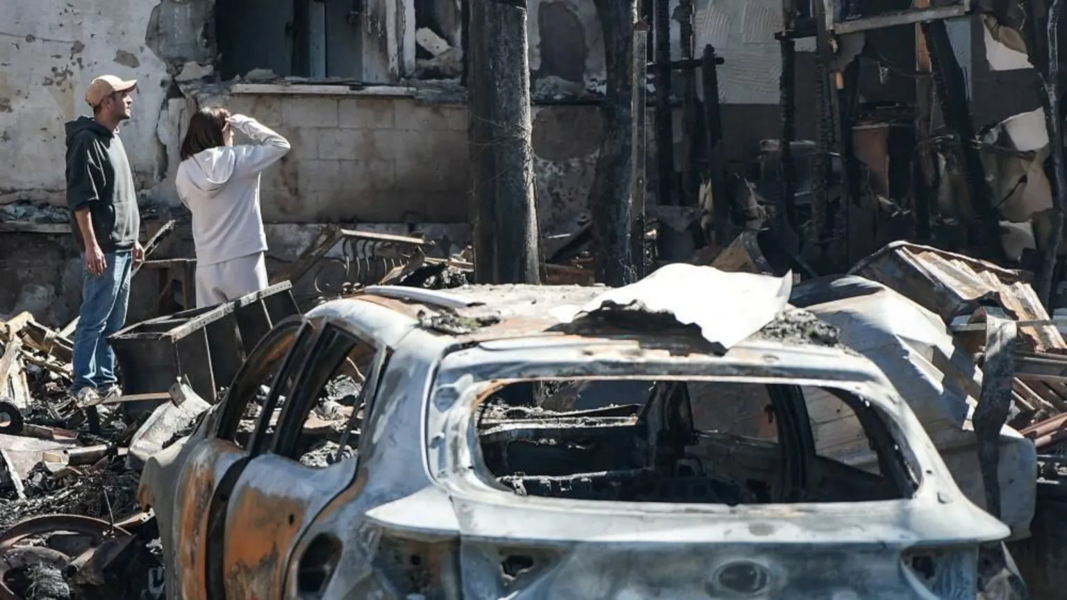 A couple look at badly damaged building, with a burnt-out car in the foreground, in Nahariya, Israel (17/03/26)