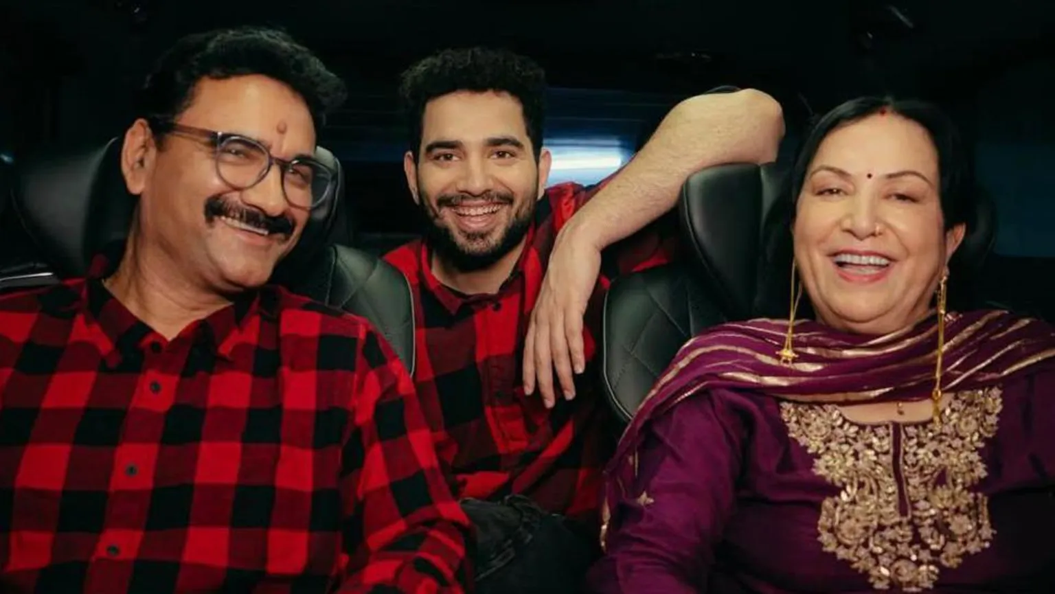 Samay Raina via Instagram Samay Raina poses gleefully with his mum and dad inside a car. He and his father are wearing matching red-black check shirts, while his mum is wearing a purple tunic and scarf with golden threadwork. 