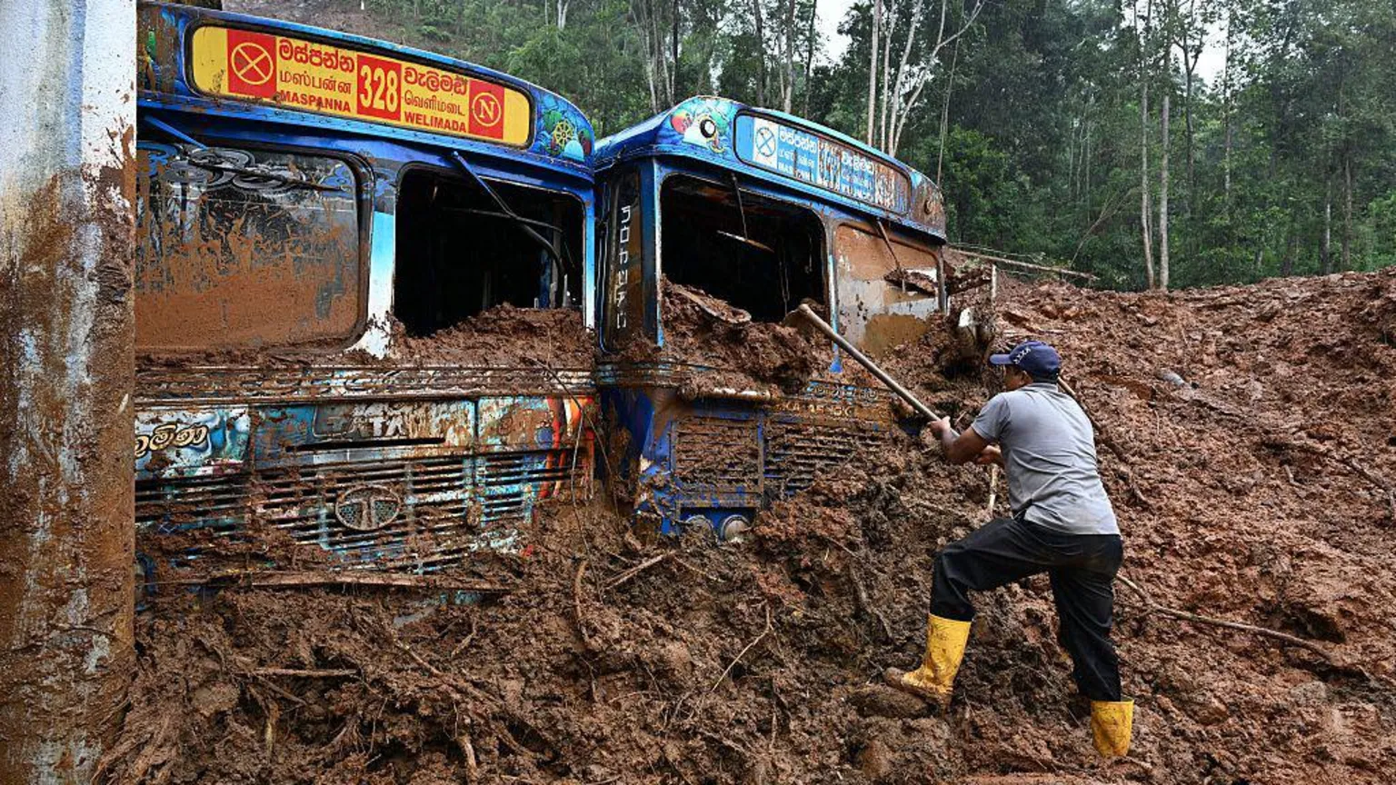 AFP via A worker removes mud accumulated around buses near a landslide-affected area in the aftermath of Cyclone Ditwah, in Maspanna on December 13, 2025.