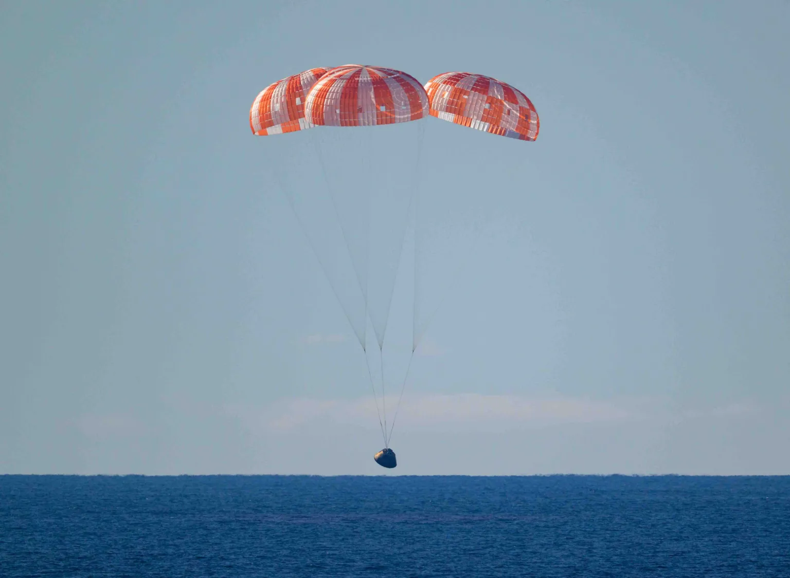 NASA The landing craft with it's orange parachutes lands on a dark blue sea.