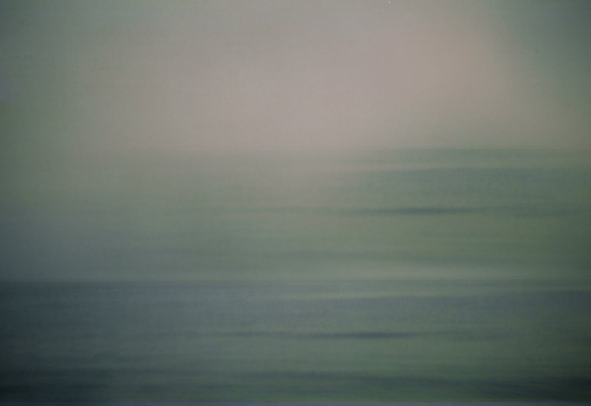A double vision of the sea: it is grey and merges with the sky as blurred horizontal lines shimmer in the light.