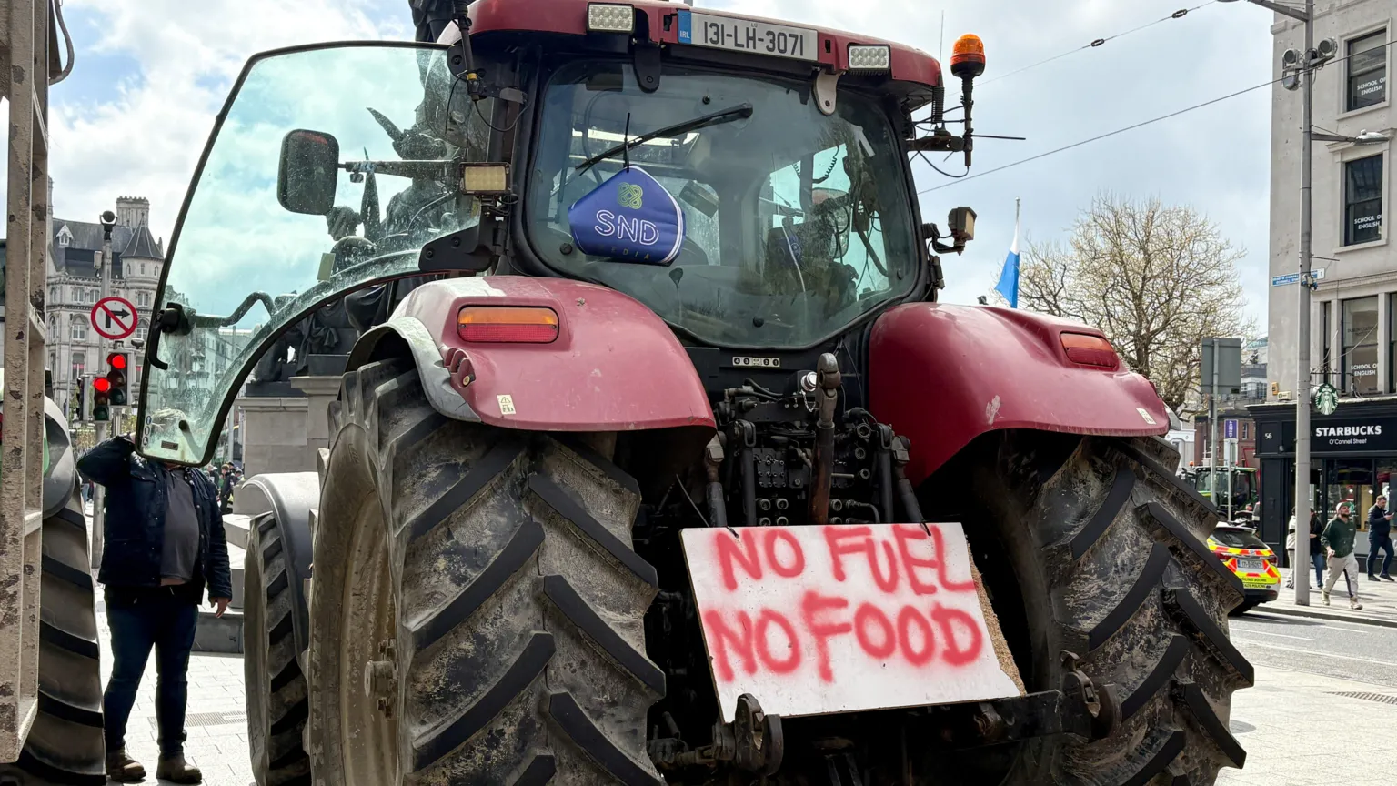 A large red tractor from behind - a white placard with red paint sits between the back wheels. The paint reads