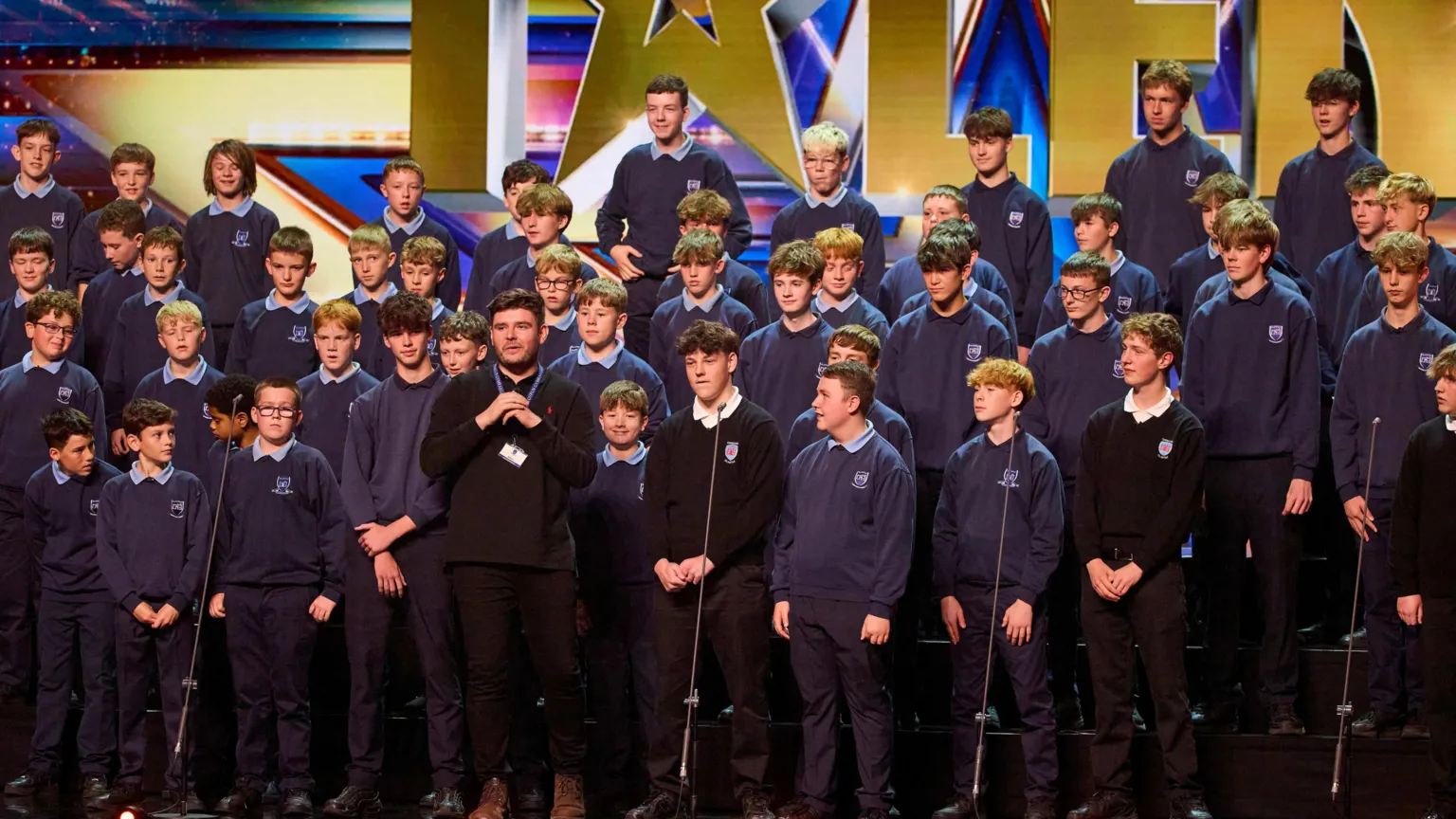 Credit BGT/TalkbackThames/ITV The choir in navy school uniform with choir leader in the middle on stage at Britain's Got Talent