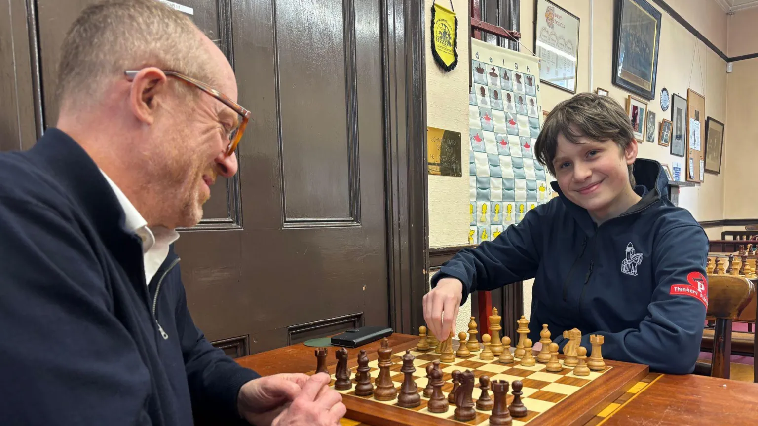 Frederick and Craig sitting at a table simulating a chess move.