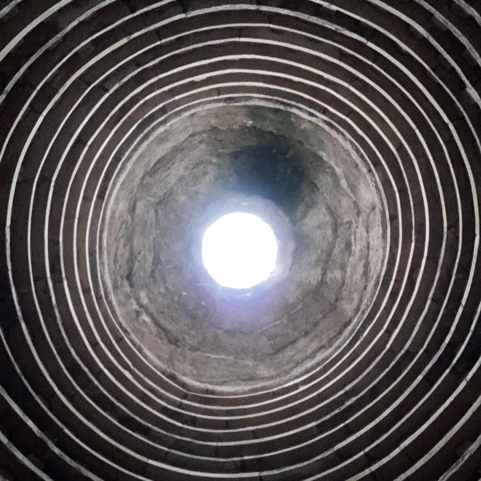Charlie Hood An upward view inside a circular stone structure, with concentric rings lining the interior walls and a bright opening of daylight visible at the top, creating a tunnel-like effect.