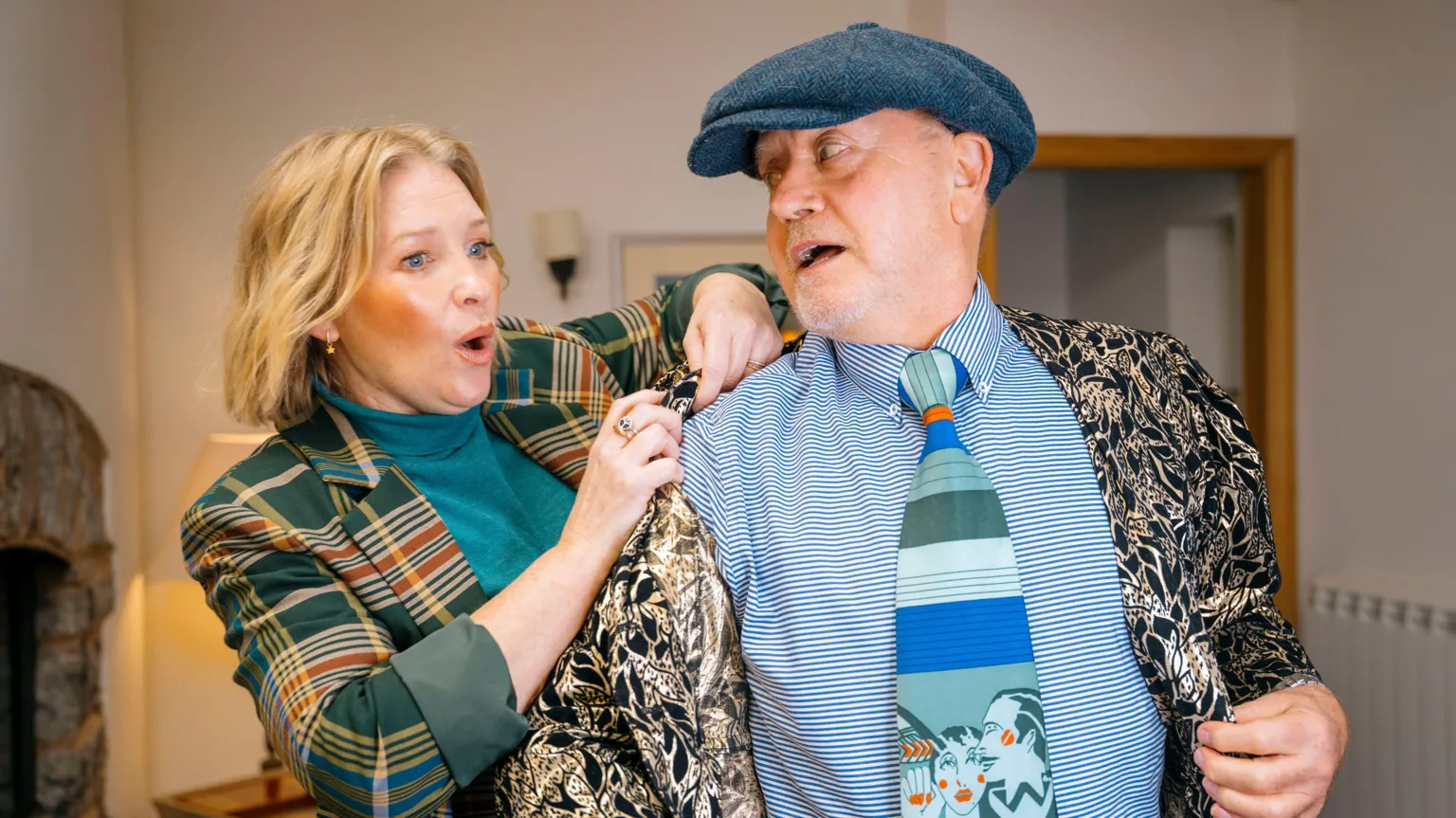 BBC/One Tribe TV Joanna Page is putting a jacket onto a man who is wearing a hat and looking at her.