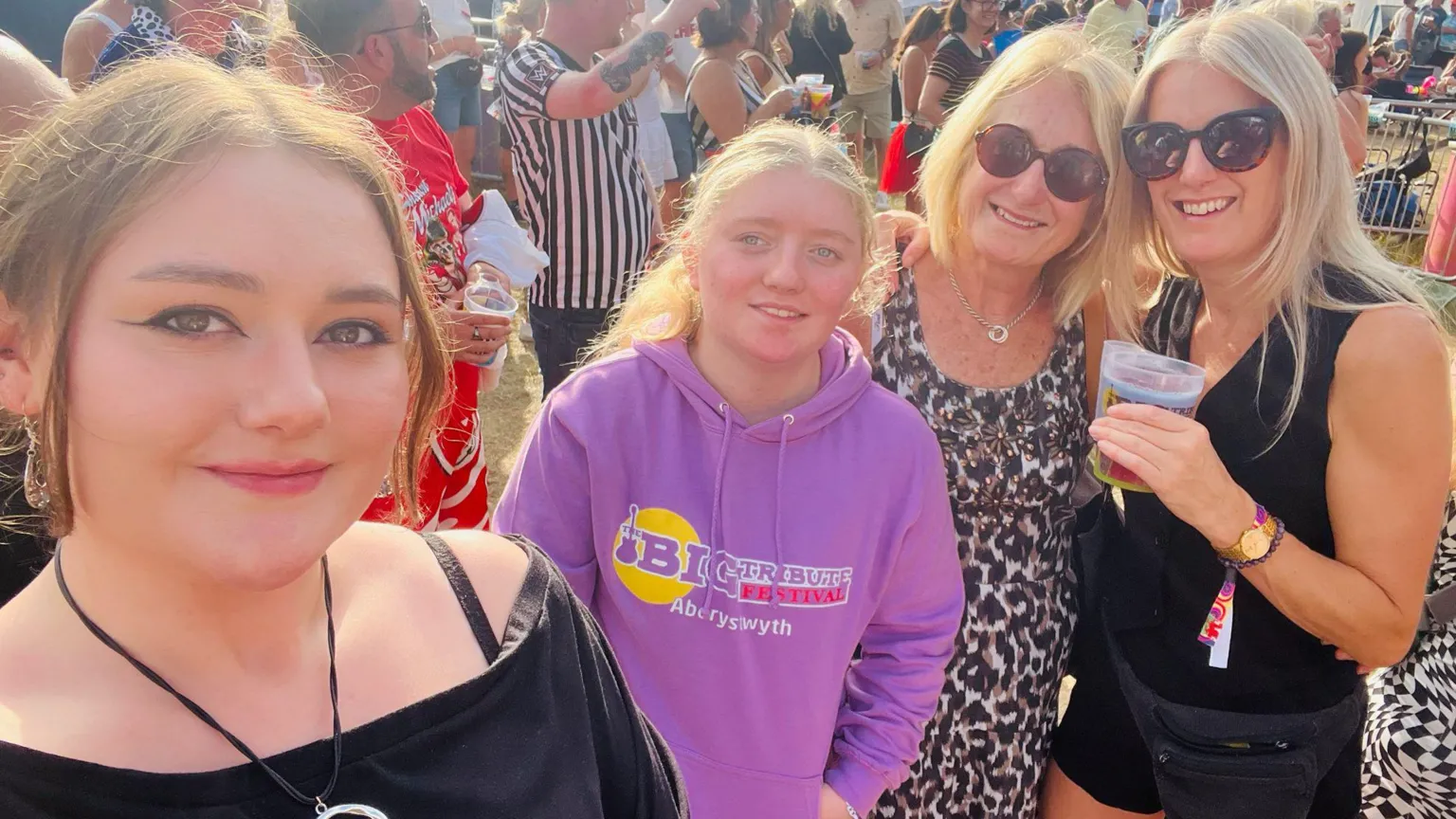 Jane Richards Helen smiling before she became unwell with her daughter and two granddaughters, wearing sunglasses and a leopard print top. They are stood at a festival in the sun, with people in the background.