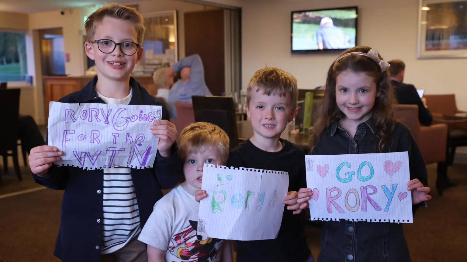 Four children smiling and holding paper notes showing support for Rory McIlroy.