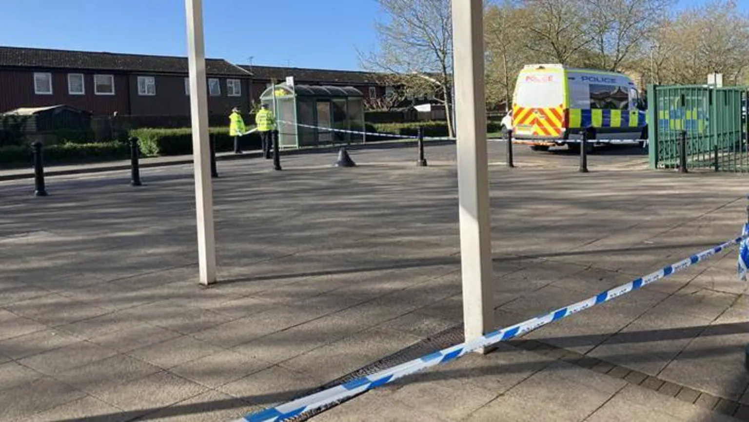 Shariqua Ahmed/BBC A police scene remains in place near a bus stop. Two officers in high-vis vests are standing in the road, and a police van and car are parked on the street. Police tape is in place.
