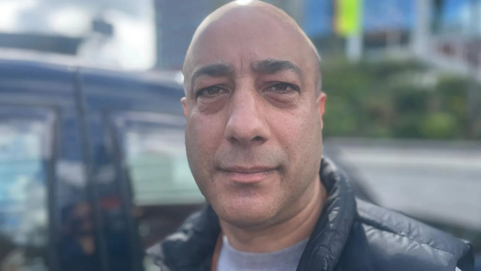Shahid Rafiq, a bald man wearing a puffer jacket stood in front of a taxi.