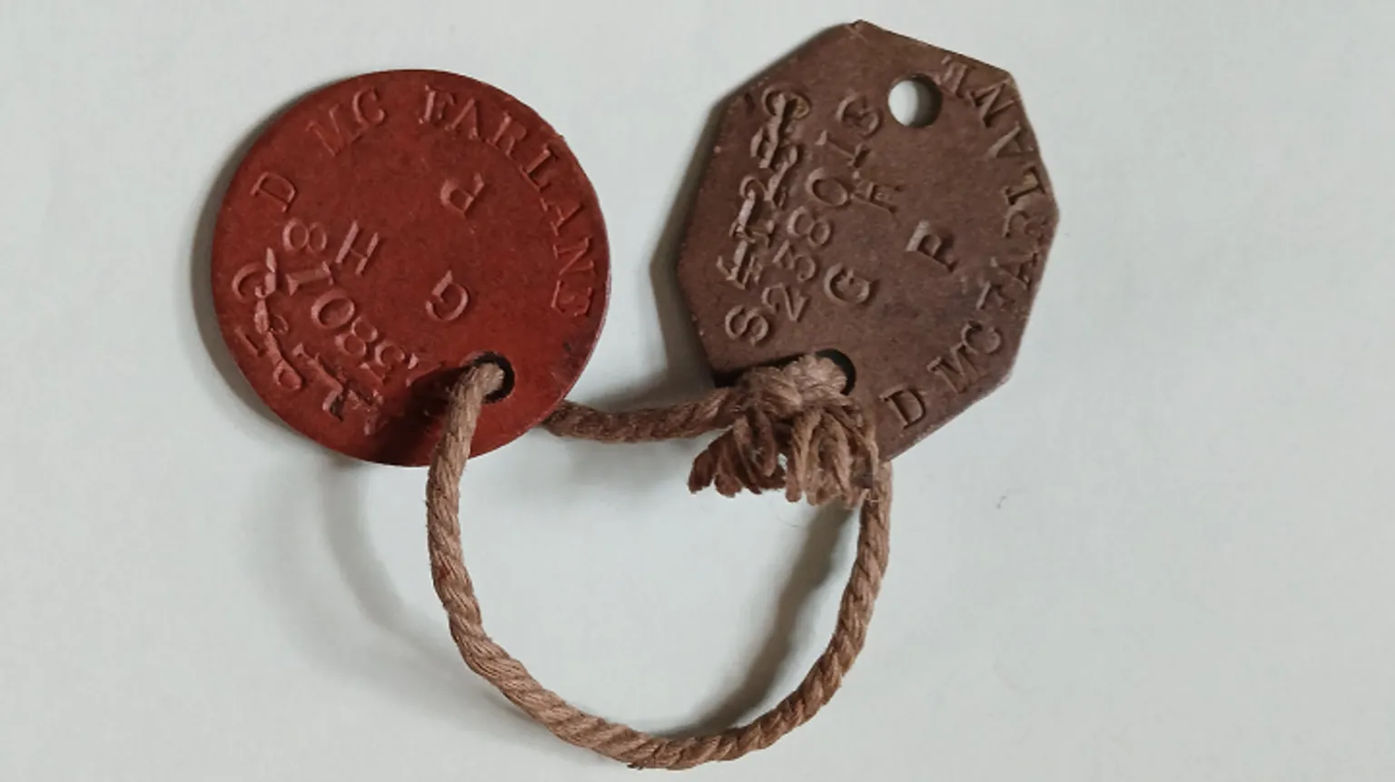 MacFarlane family Two brown-coloured identification tags displaying the text D MCFARLANE, joined by a small piece of string.