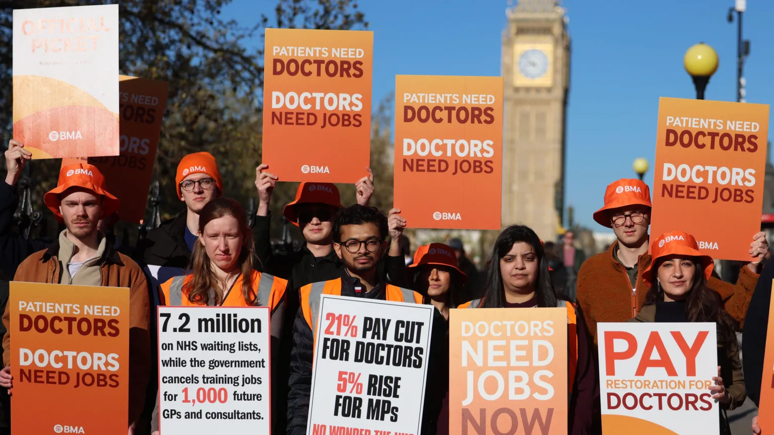 EPA A group of resident doctors stand in a line holding orange BMA placards - Big Ben is in the distance