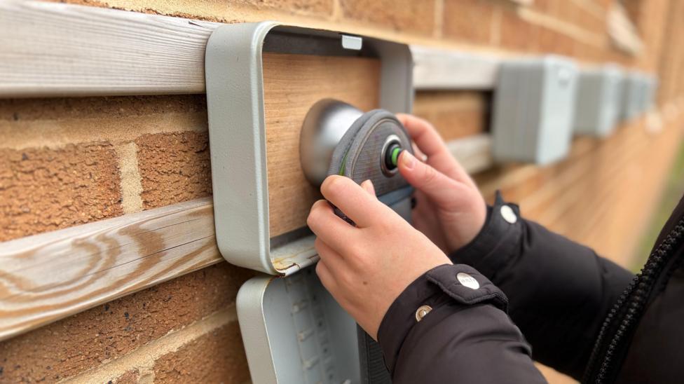 Bag arbennig ar cyfer cadw ffonau yn cael ei rhoi gan ddisgybl ar declyn ar y wal gyda magnet i agor y sach