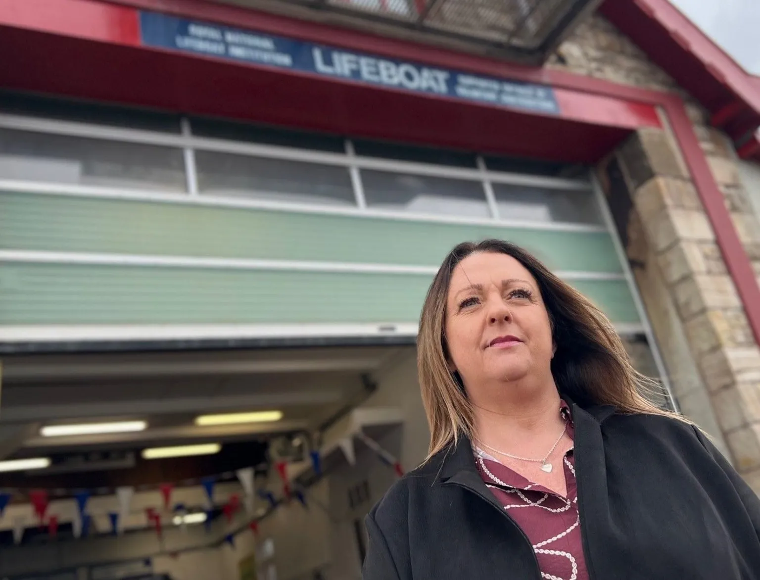 A woman looks out to the distance with a lifeboat station behind her