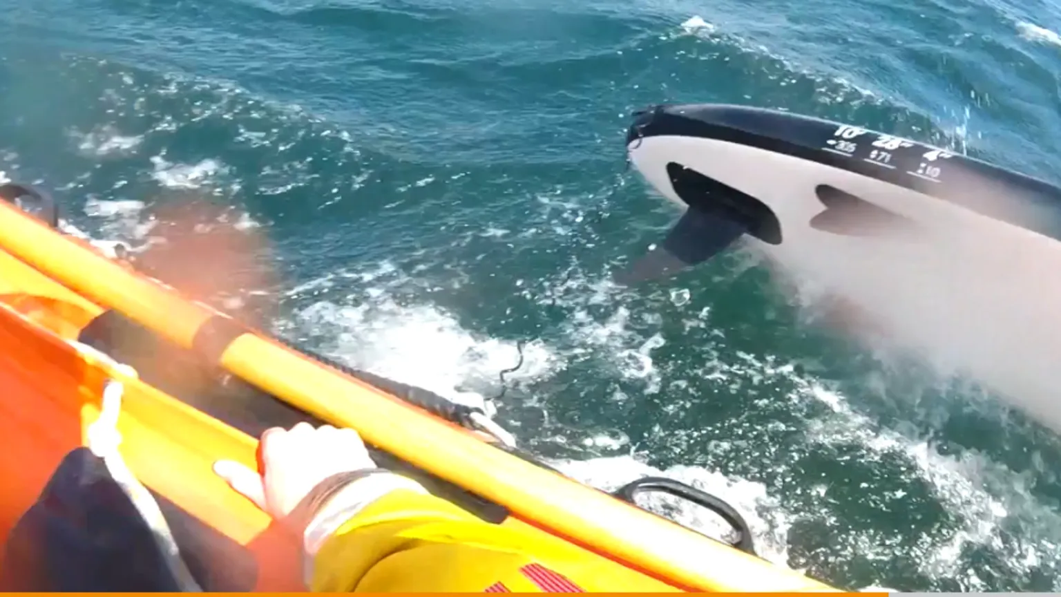 RNLI A blue and white paddleboard in the sea next to a lifeboat, with a crew member's hand visible