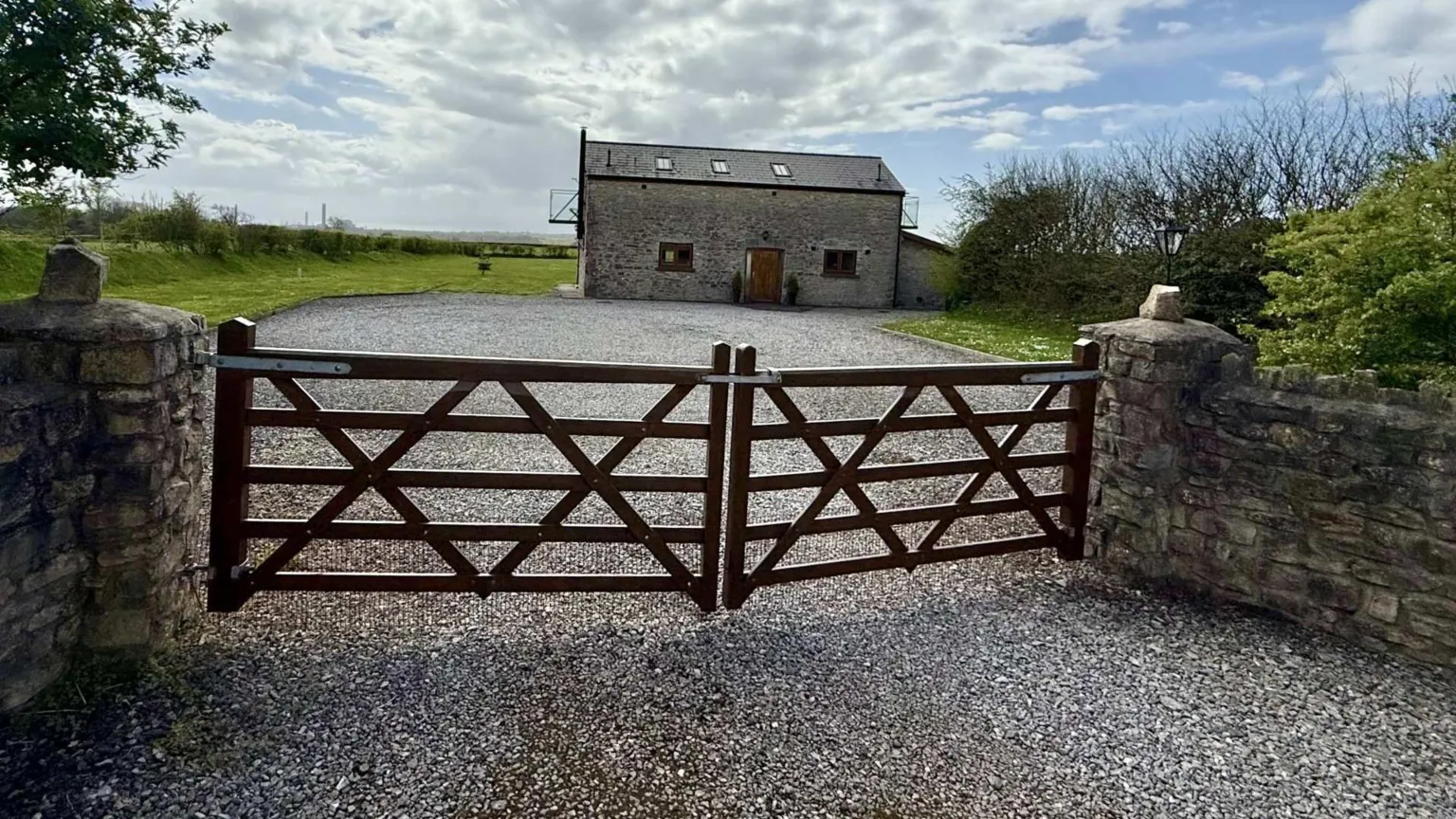 Stone yard with a gate. Behind the gate is a grey brick cottage with two small windows and a brown front door. The roof of the cottage has three small windows. There is two balconies either end of the property. 