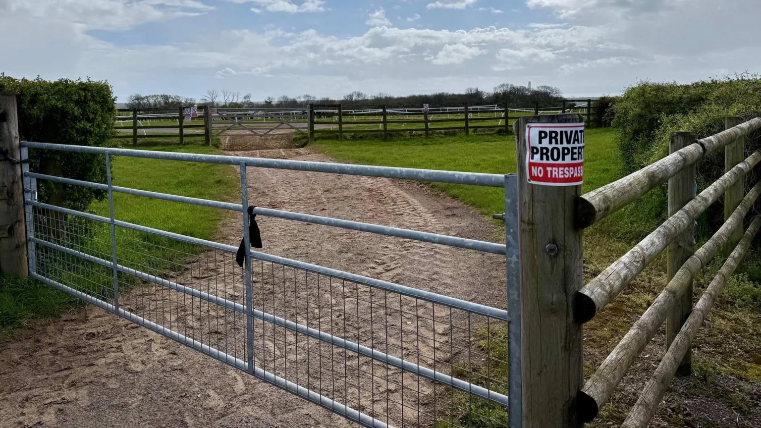 Fields with wooden and metal gates. There's a white and red sign that says 'private property' and 'no trespassing'. 
