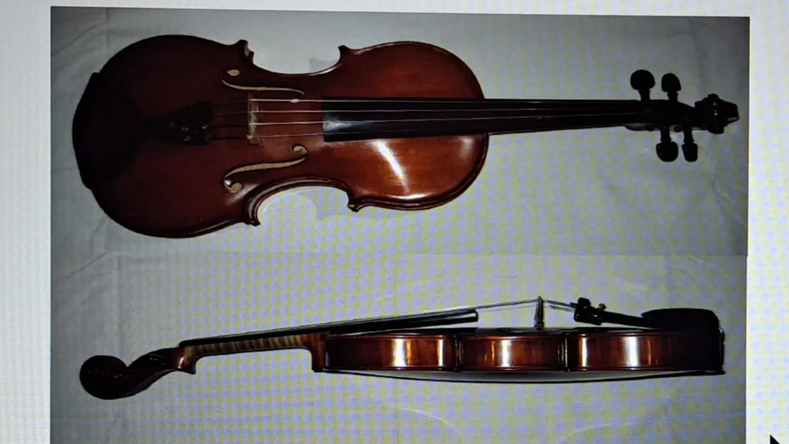 Joseph Maher Photo of the violin - a brown shiny instrument with strings and pegs. It is pictured from the side and from the top in two separate shots. It seems to be lying on a checked sheet. The sort of image you'd provide for insurance purposes.