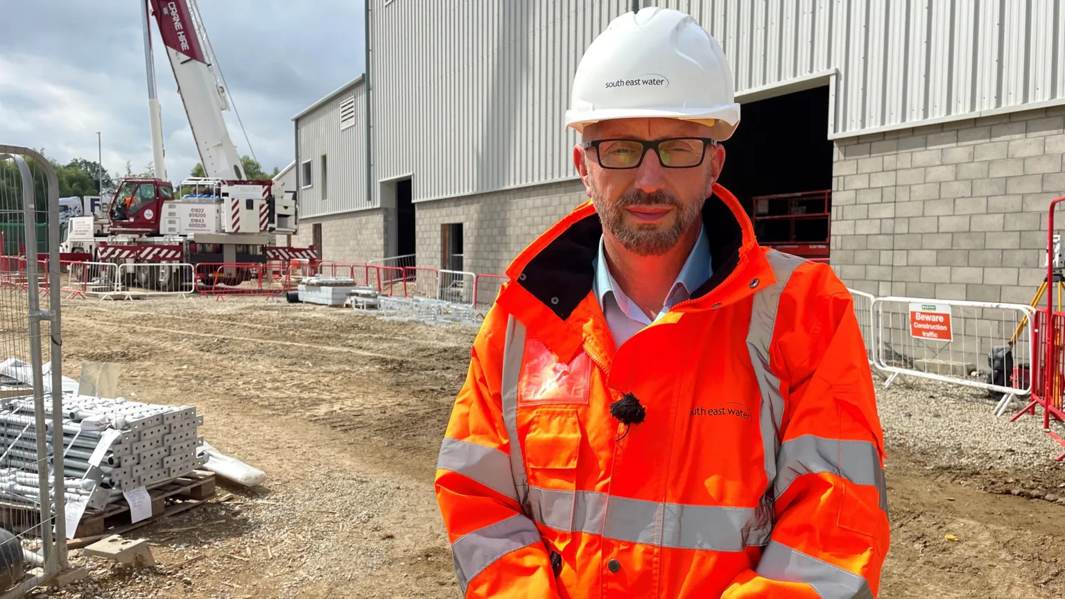 BBC/Yvette Austin A man wearing an orange hi-vis jacket and a white work and safety hat. He is standing in a construction area.