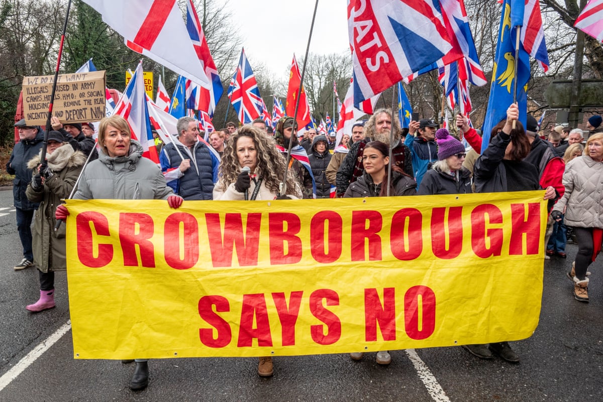 People march down the street waving Union flags and holding up a big banner that says: Crowborough says no