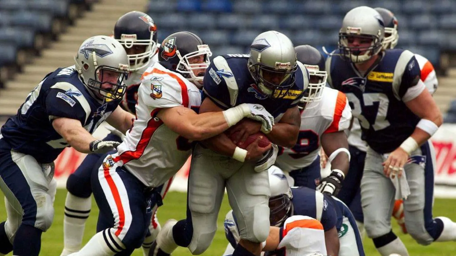 SNS A Scottish Claymores game, with the team's running back holding the ball and trying to fight off a tackler, as other players watch on