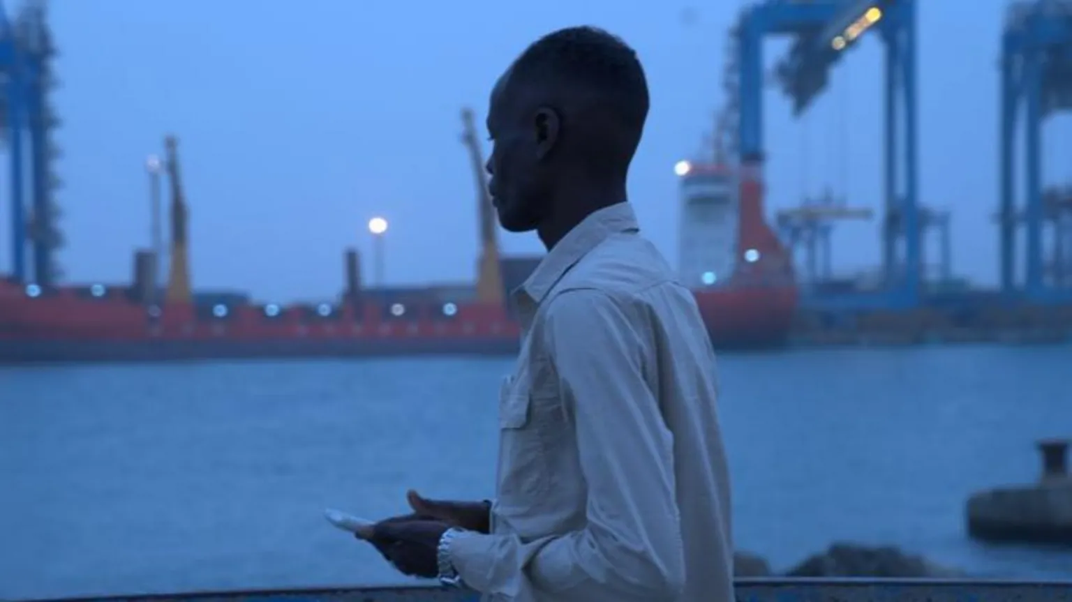 Mohamed Eid Mohamed Suleiman, with a phone, looking into the water in Port Sudan