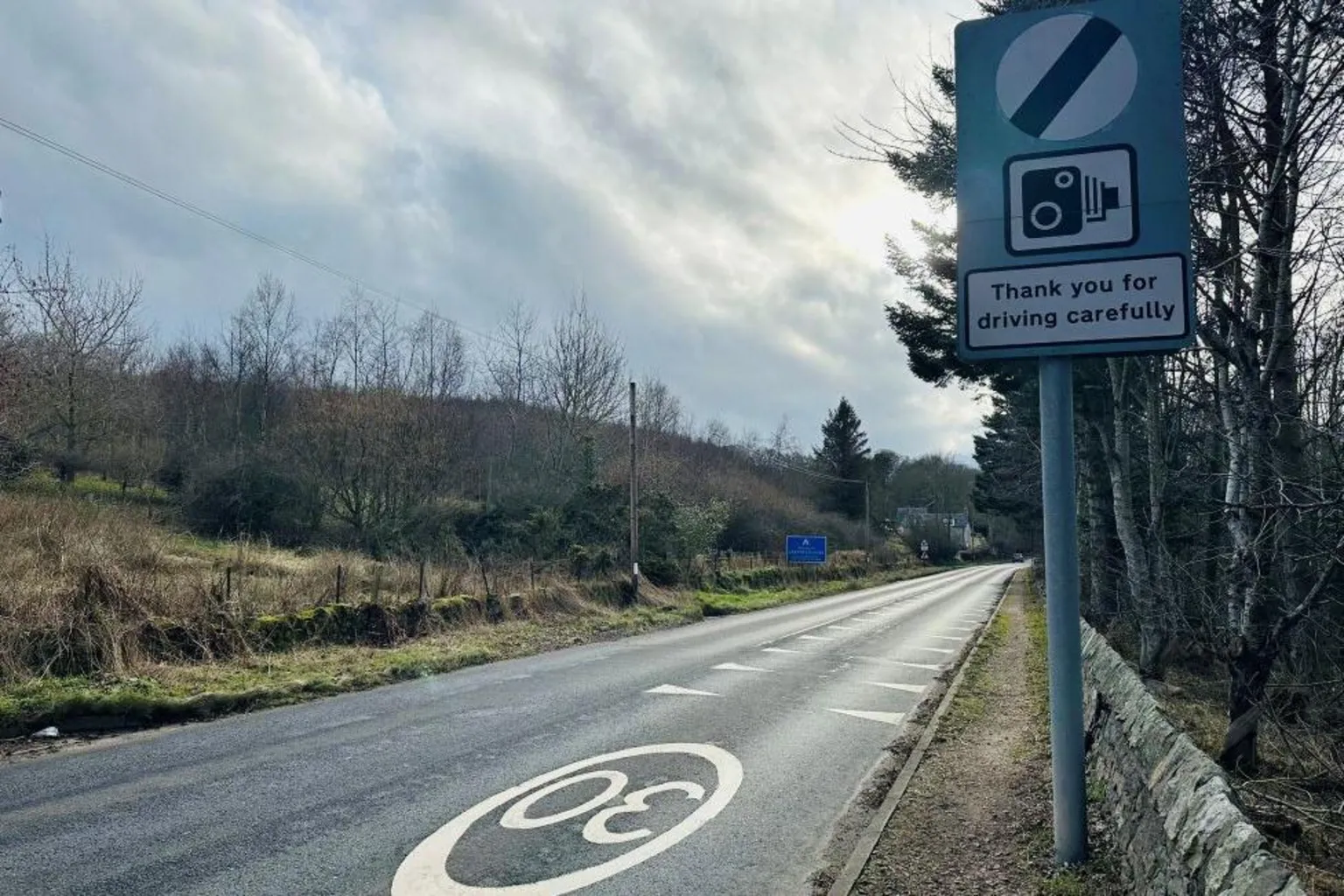 A rural road with a 'thank you for driving carefully' sign.