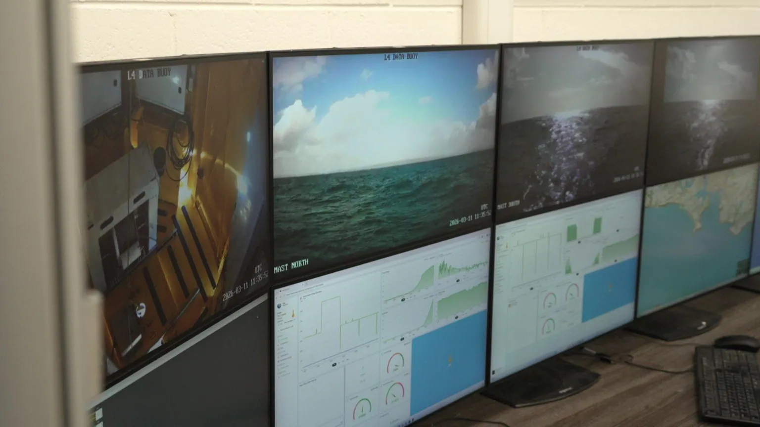 Screens with different images on them. The top four screens have images of the sea and the bottoms screens have imaged of data and a map. The screens are on a brown desk.