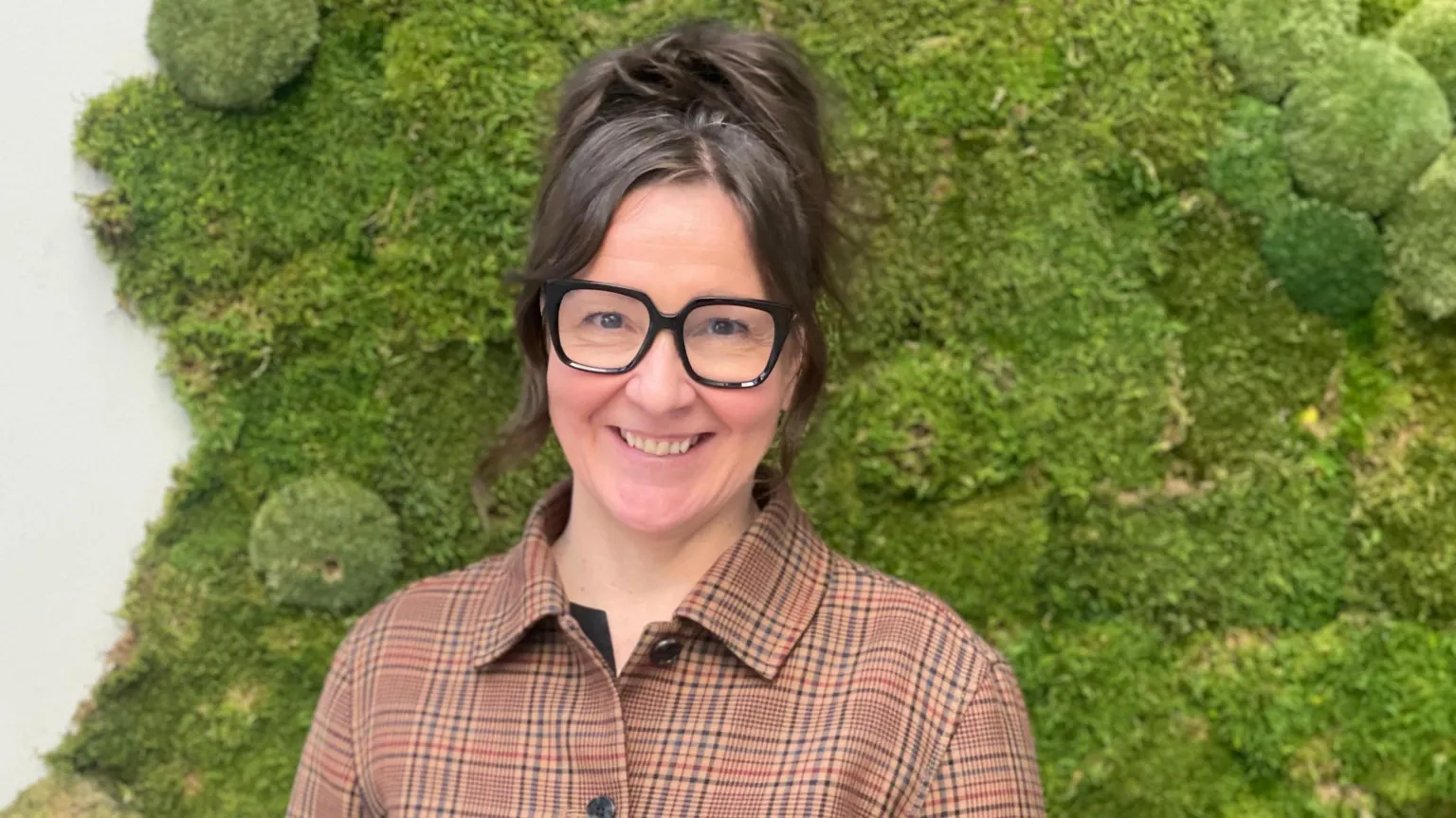 Maddy Savage Jannie Jeppesen smiles at the camera, wearing a patterned top and thick framed, black glasses