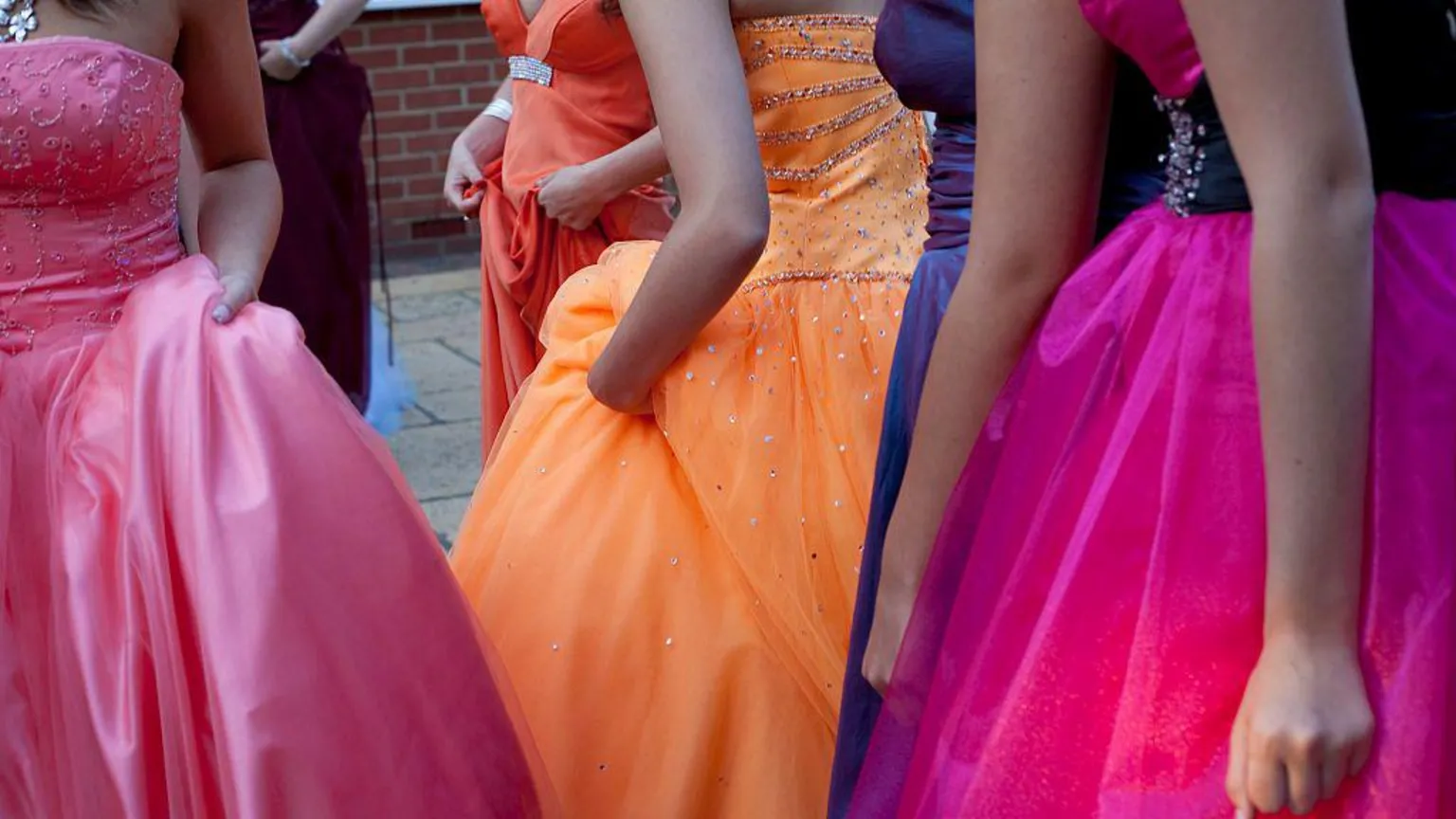 Girls at a school prom wearing pink, purple and orange prom dresses.