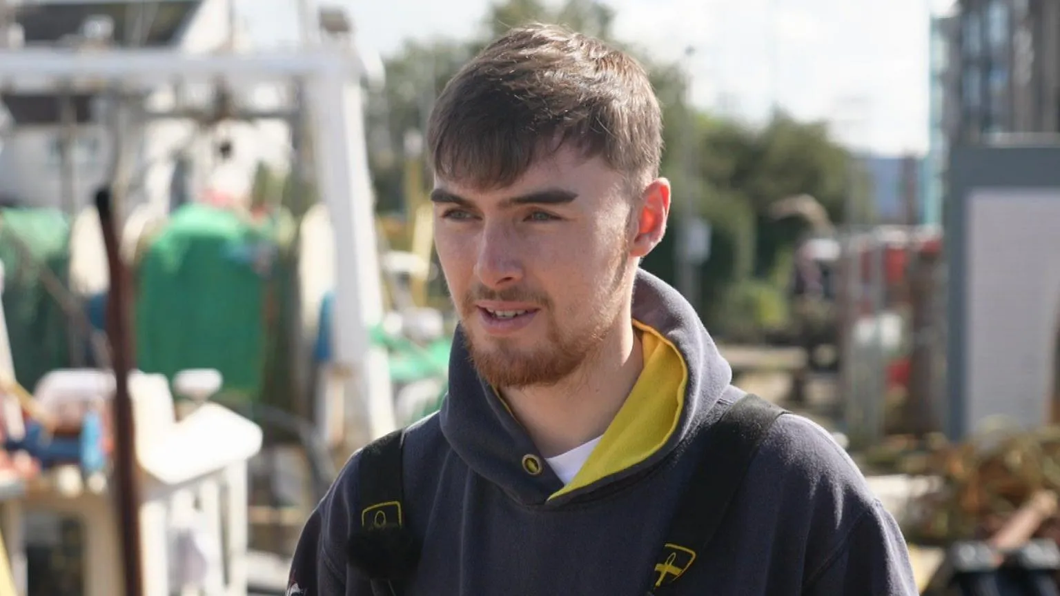 Joe Lynch looking to the left and wearing a blue hooded jacket. He has short brown hair and a short beard. 