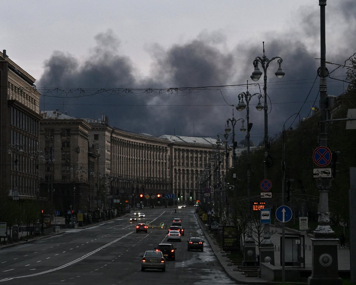 Cars drive along Khreshchatyk Street as smoke rises above buildings in the background following an air attack in Kyiv.