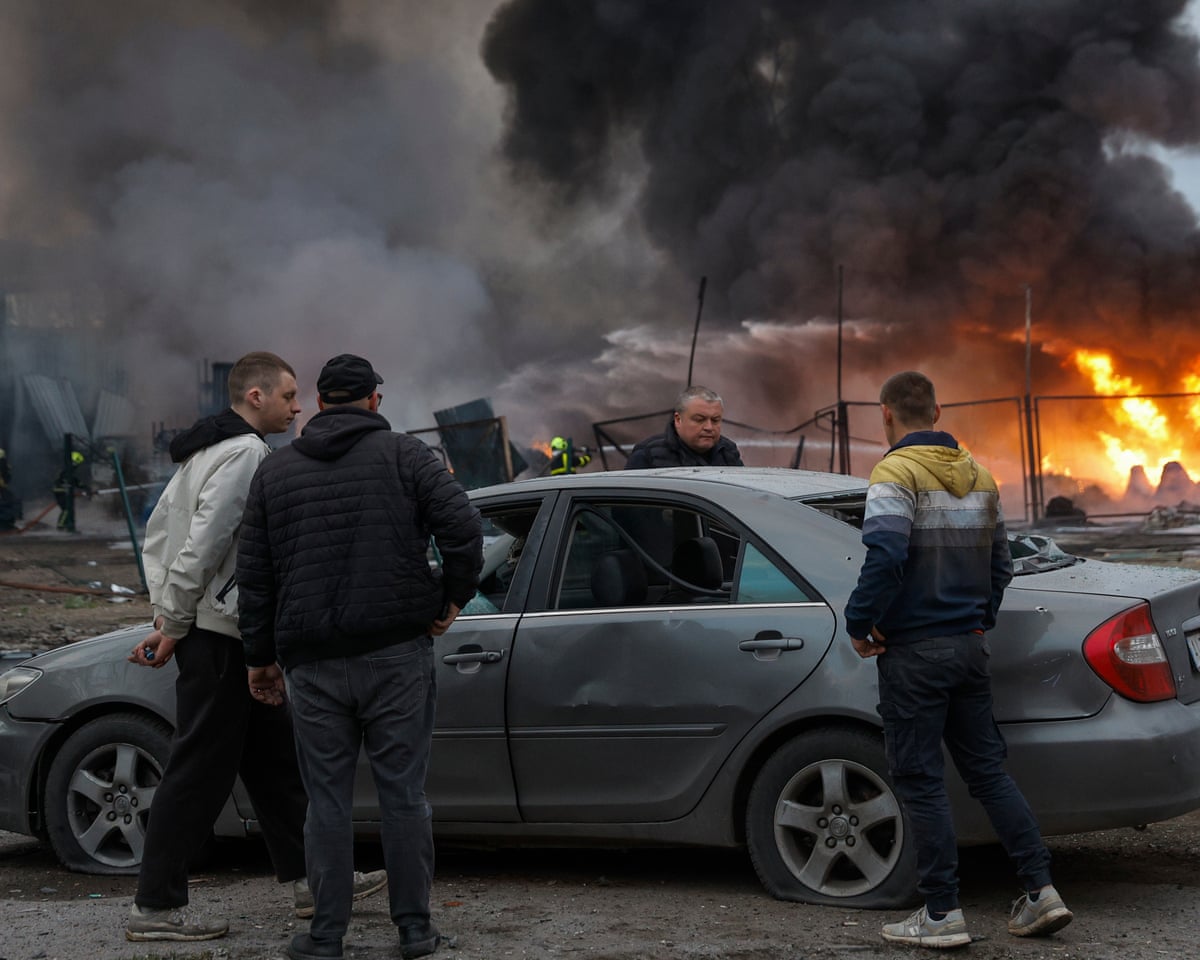 Local people react near a damaged car at the site of a Russian strike on a civilian storage facility in Kyiv, Ukraine.