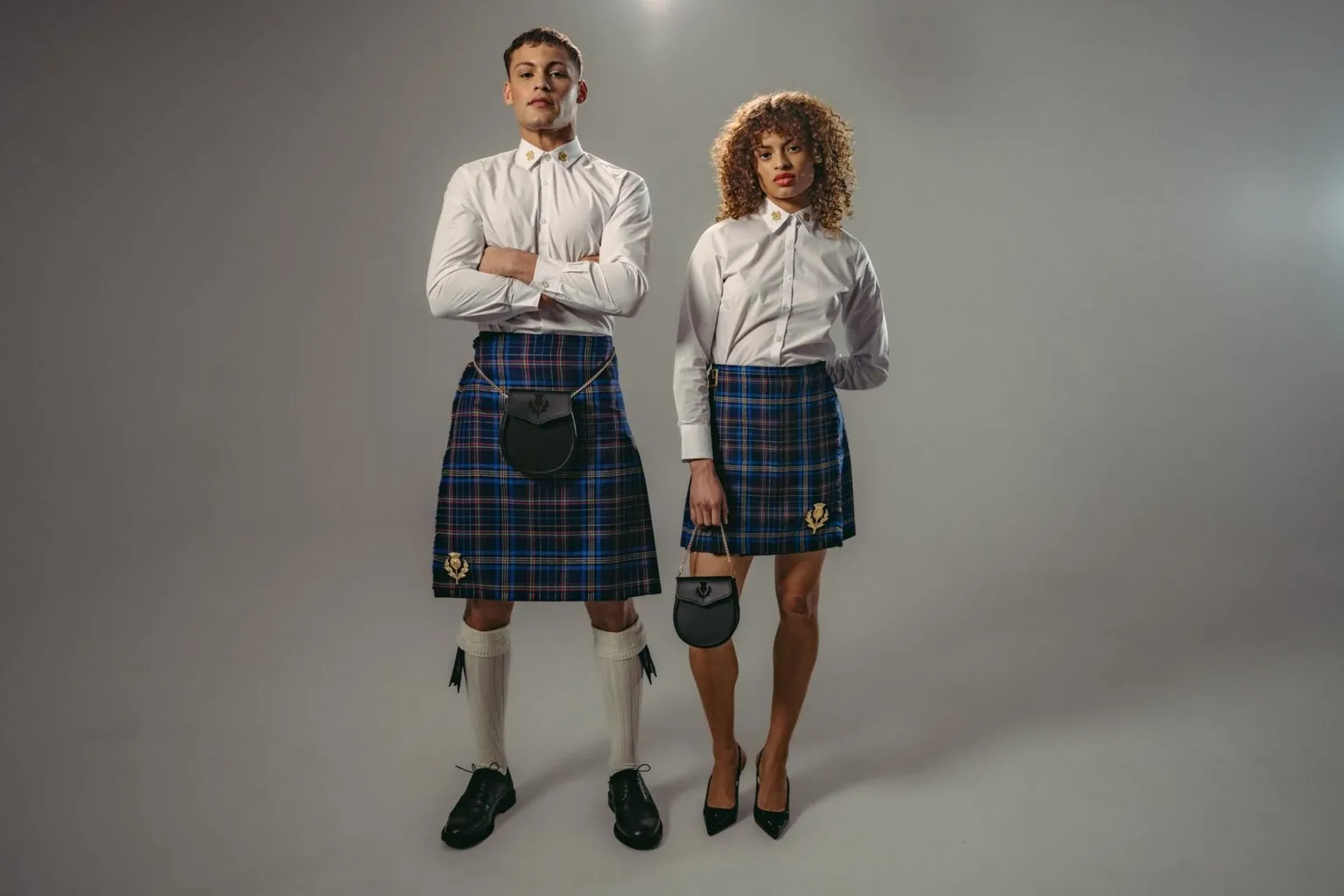 Team Scotland A male and female model in the Team Scotland uniform - blue tartan kilts and white shirts. The man is wearing a black sporran and the woman is carrying a small black bag. They both have black shoes on and he is wearing long, white socks with black sock flashes.