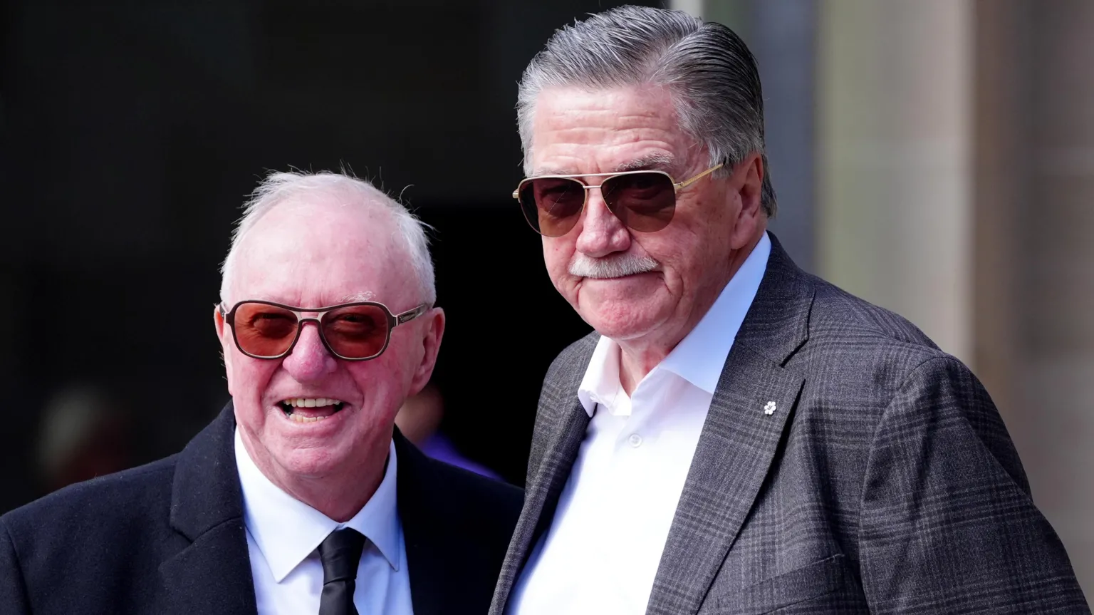 Dennis Taylor and Cliff Thorburn, two men with grey hair both wearing sunglasses, smiling for a photo outside Sheffield Cathedral.