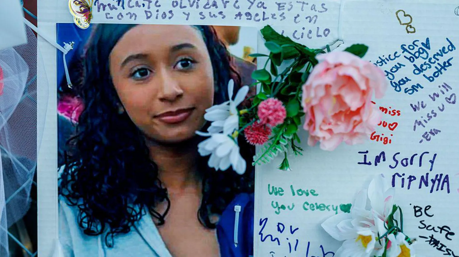  Photo of young woman with long wavy black hair surrounded by messages in Spanish and English written around it on a white board, and flowers pinned in places 