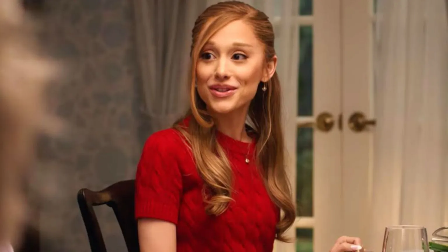 Universal Ariana Grande in Focker-in-Law, wearing a red sweater and sitting at the dinner table