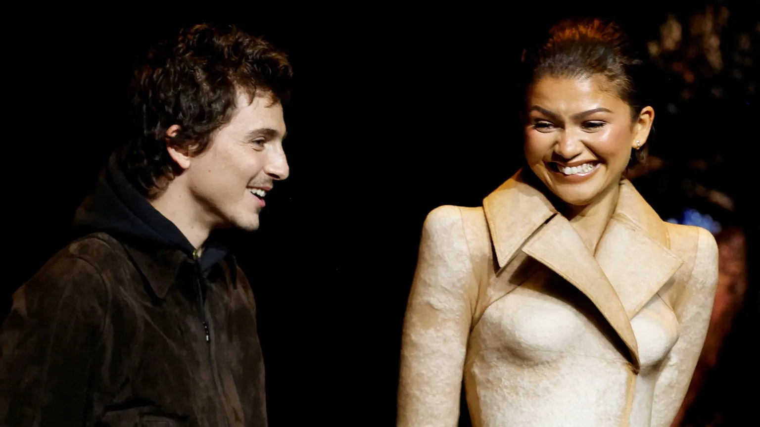  Timothee Chalamet and Zendaya standing and smiling on stage