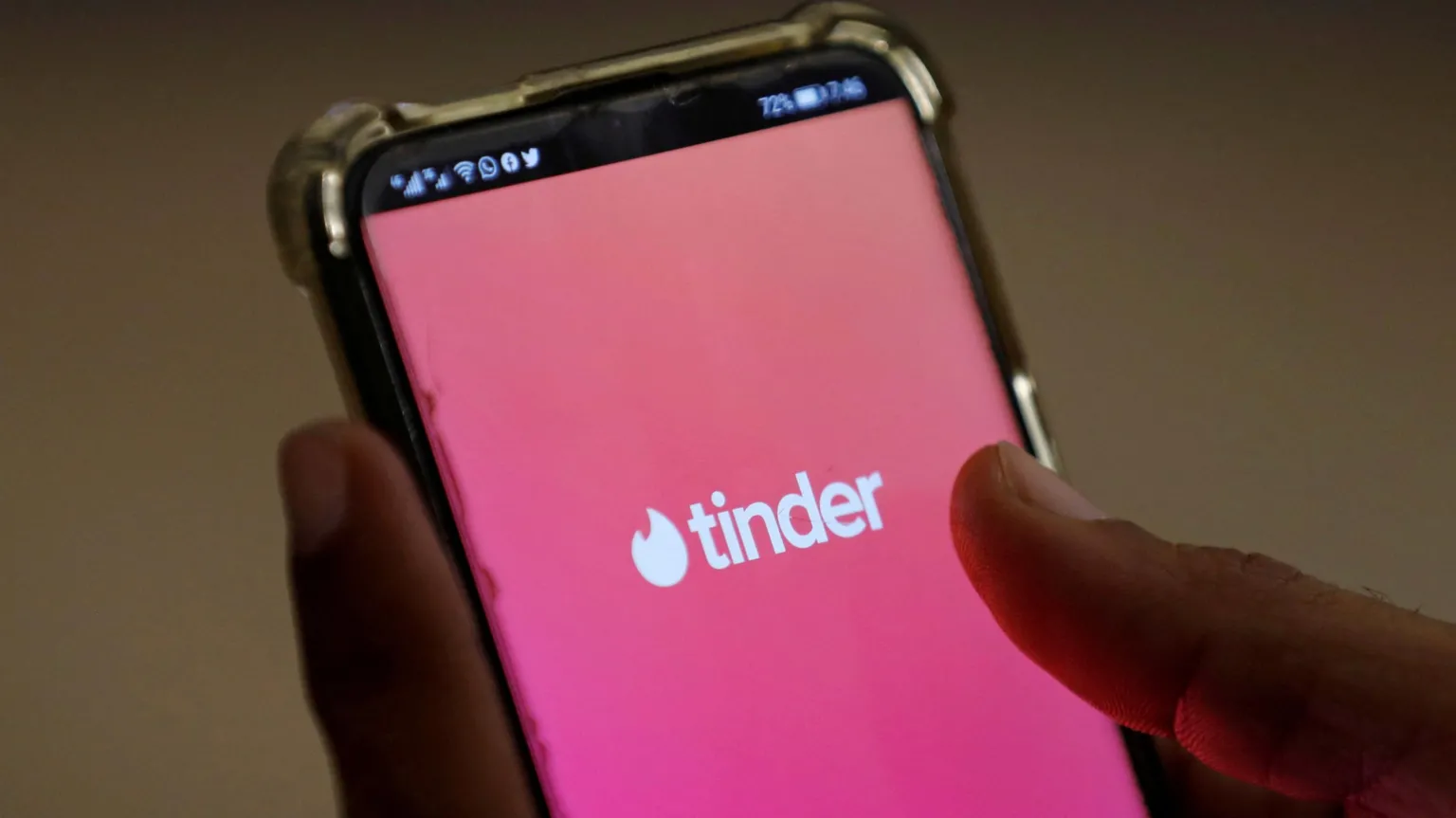  Close up of a person's hands holding a smartphone with the Tinder logo in white text on a pink background filling the screen