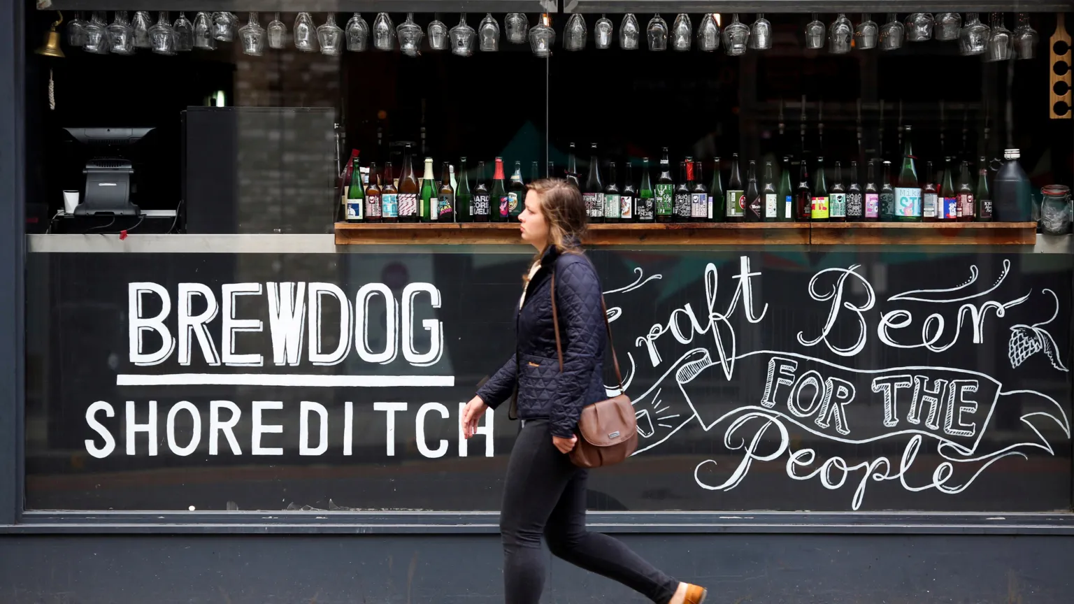  A woman walks past a Brewdog bar in London. On the glass is written Brewdog Shoreditch and Craft Beer for the People.