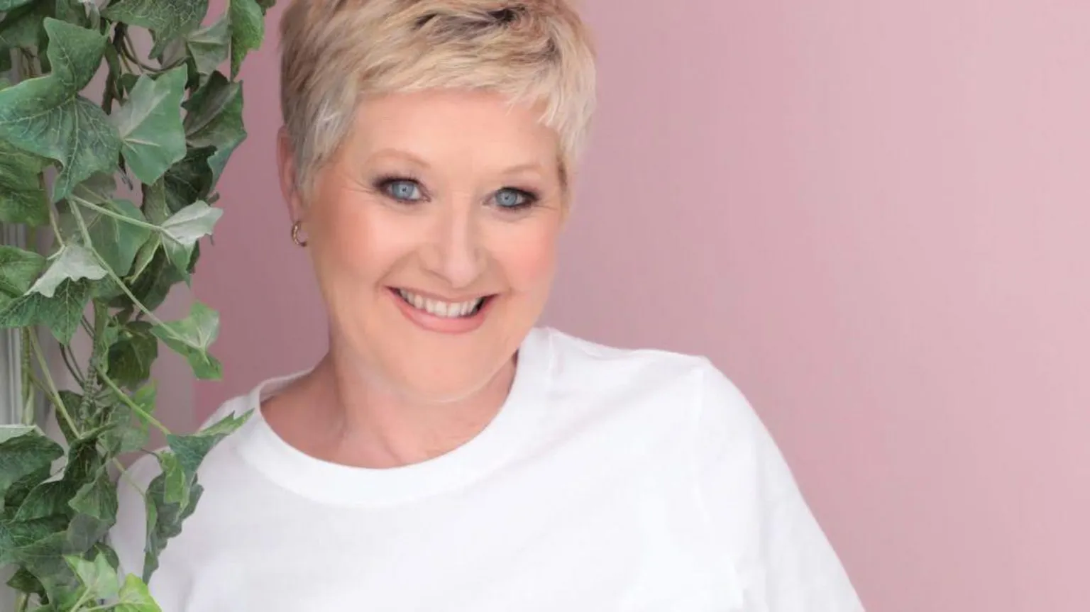 Jennifer Bradnam Jennifer Bradnam smiles at the camera as she stands in front of a pink background, with a green plant next to her. She has short blonde hair and wears a white T-shirt. 